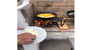 The cooking experience begins with the use of a frying pan placed over a wood fire